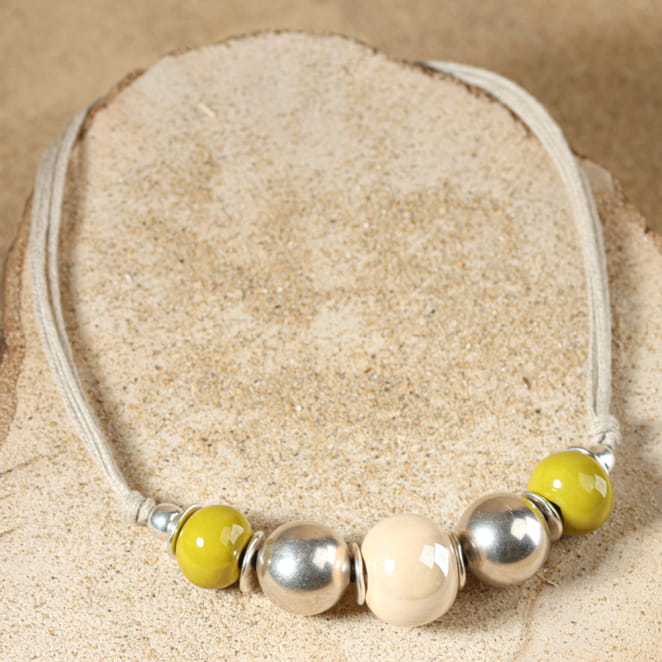 collier Ancolie argenté avec perles jaunes et multicolores disposé en cercle sur fond sable