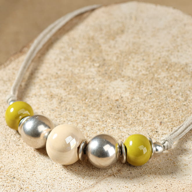 collier Ancolie argenté avec perles jaunes et multicolores présenté sur fond sable