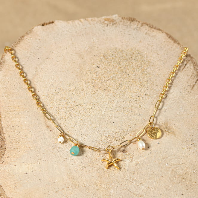 collier Dolcevita doré avec pendentifs vert d’eau sur sable clair