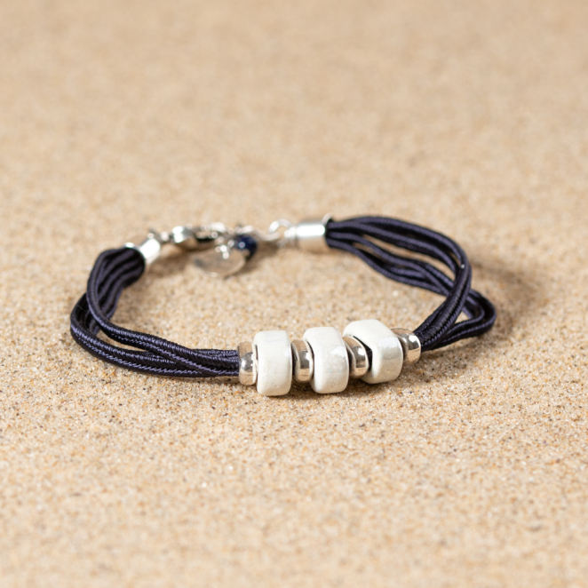 Bracelet Ceram posé sur le sable, contraste élégant entre blanc, noir et argent.