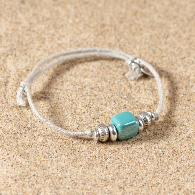 Bracelet posé sur le sable, contraste entre le vert intense et l’argenté délicat.
