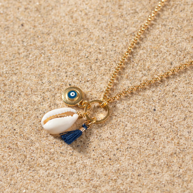 Collier Grèce posé sur le sable, chaîne fine dorée et breloque inspirée par la mer Égée.