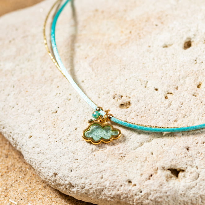 Mochi est un collier pour enfant turquoise composé d'un pendentif en forme de nuage à paillettes et d'un cordon en coton turquoise.