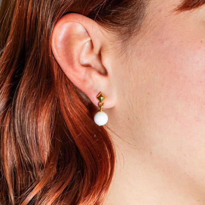 Atome est une paire de petites boucles d'oreilles composée d'un clou d'oreilles en métal doré d'un flash d'or 24 carats et d'un pendentif boule blanc. Il s'agit d'une pièce unique fabriquée sur l'ïle d'Oléron.