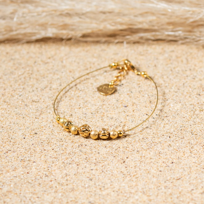 Bracelet Leslie posé sur le sable, reflet doré et élégance naturelle.