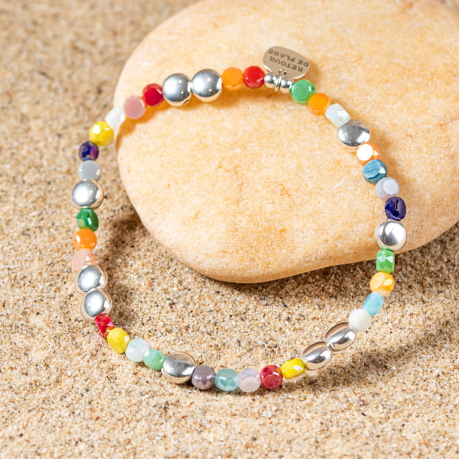 Bracelet artisanal posé sur le sable, mix coloré évoquant les vacances.