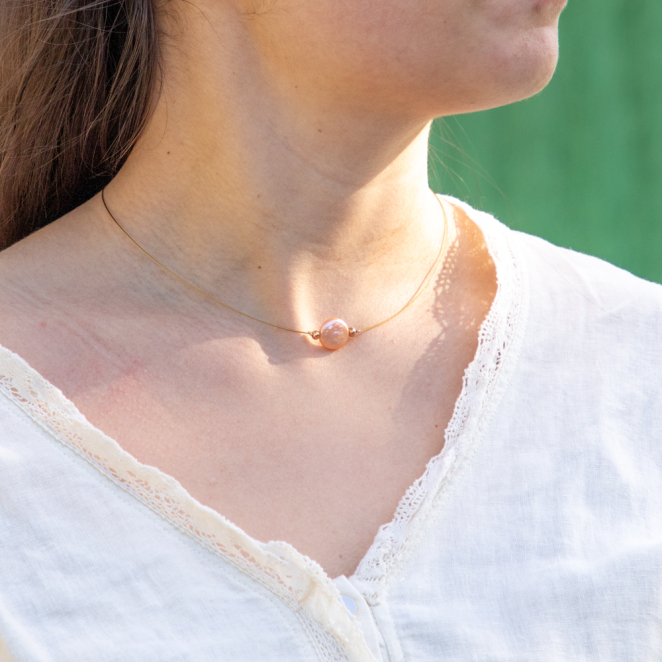 collier Flamand doré, avec pendentif rose saumon en forme stylisée, porté sur fond uni