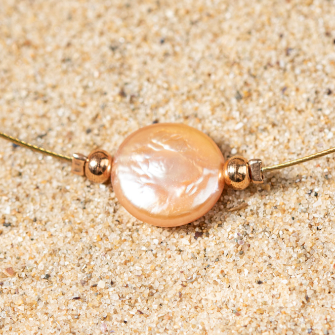 collier Flamand et son pendentif en verre rose saumon sur le sable, reflet lumineux