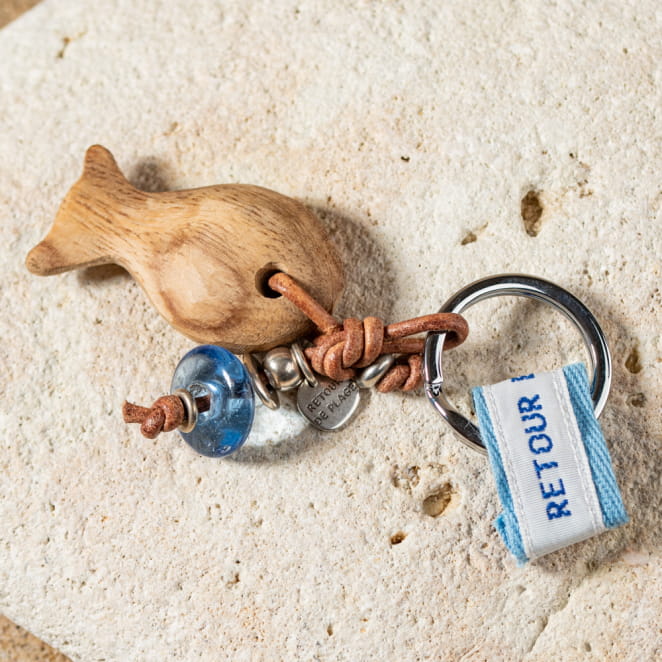 Porte-clefs If : composé d'un poisson en bois, d'un cordon en cuir marron, d'une perle en verre recyclé bleu plate et d'une perle argentée ronde.