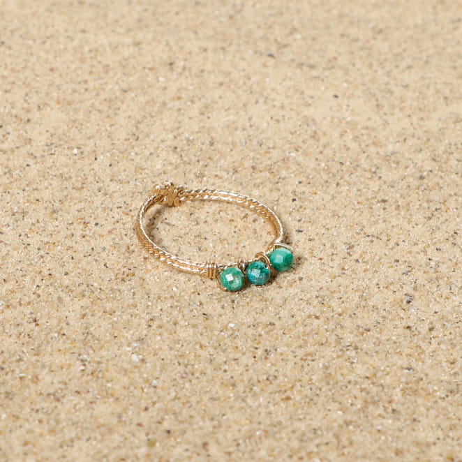 bague Nantaise dorée ornée d’une pierre turquoise posée sur sable clair