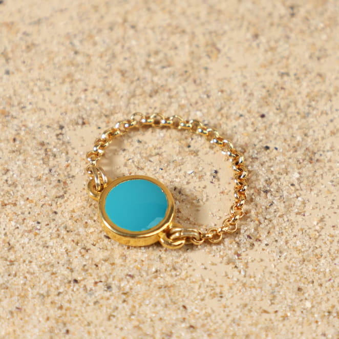Bague Ouest dorée bleu turquoise posée à plat, montrant sa fine chaîne en métal doré à l'or fin 24 carats et son médaillon rond émaillé bleu vif, création artisanale française de Retour de Plage.