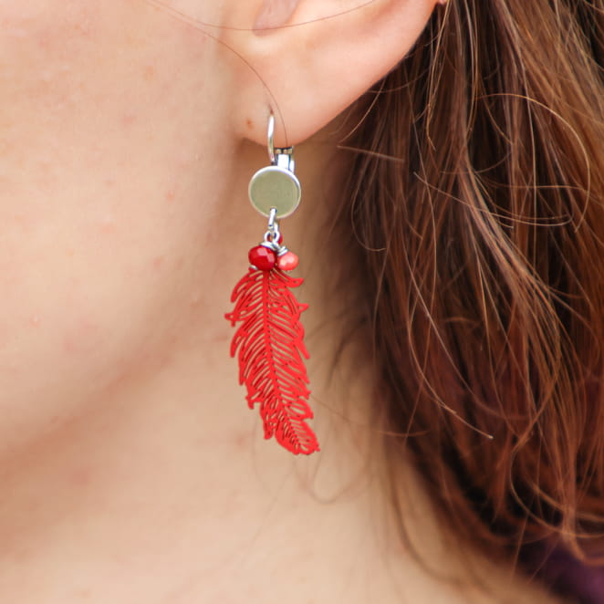 Vue rapprochée des boucles Ara rouge, avec perles et plume stylisée – fabrication artisanale