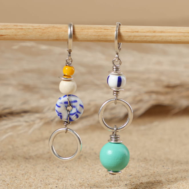 boucles d’oreilles Bariolé argenté ornées de perles émeraude et multicolores posées sur fond sable