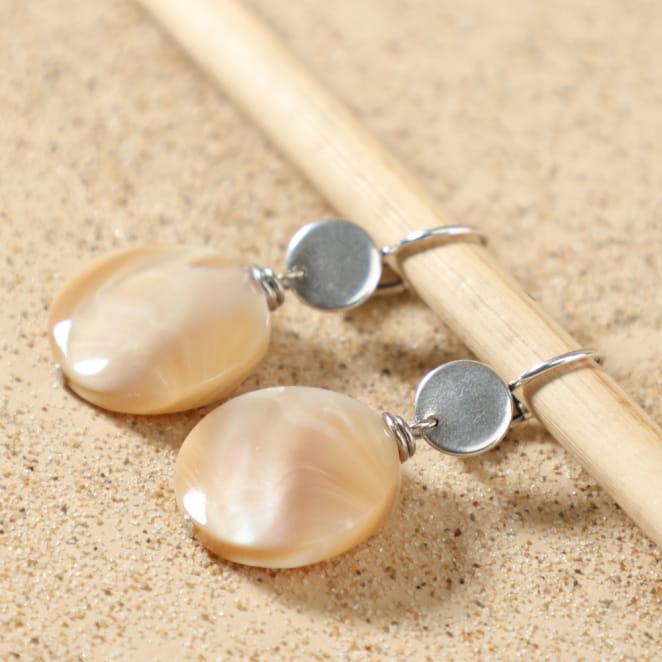 Boucles d’oreilles Calanque argentées posées à plat, montrant leur design élégant avec perle ronde en nacre beige, fait main en France – Retour de Plage