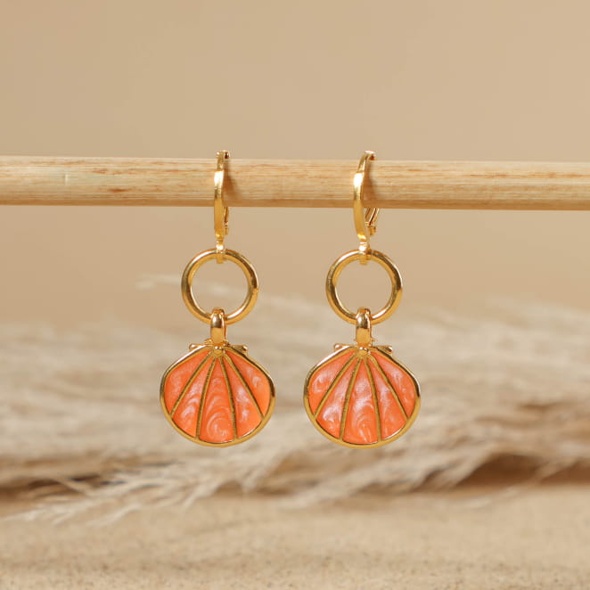 boucles d’oreilles Caliope doré avec perles corail posées sur fond sable