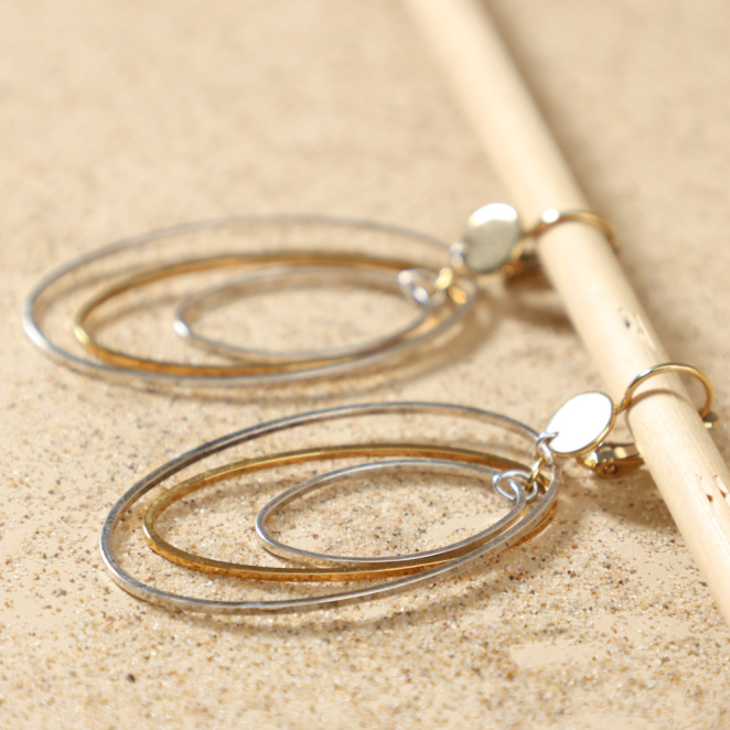 Boucles d’oreilles Proton argentées et dorées posées à plat, illustrant leur design élégant et contemporain avec trois anneaux ovales imbriqués, fait main en France – Retour de Plage