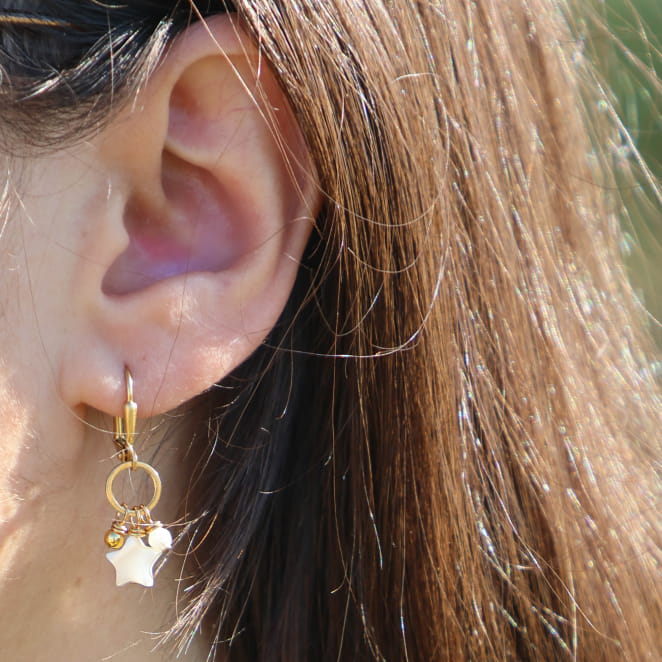 Boucles d'oreilles Véga portées – bijou en métal doré avec étoiles et perles en nacre blanche, fabrication artisanale française
