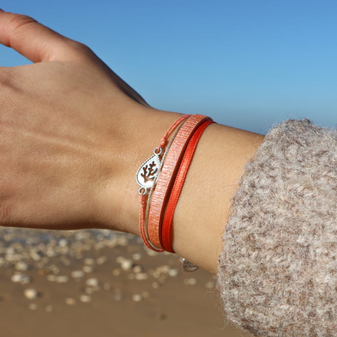 Bracelet en métal argenté, perles corail lumineuses, porté au poignet avec fil noué.