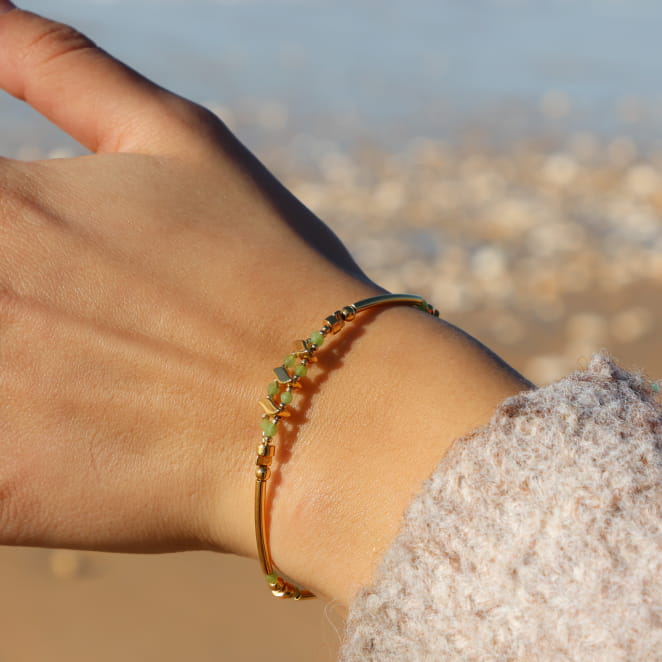 Bracelet doré orné de perles vertes lumineuses, au design délicat et artisanal.