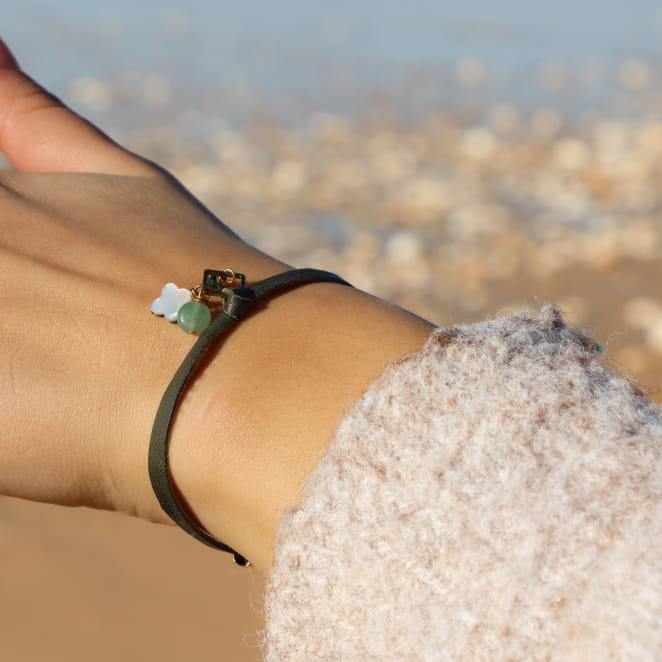 Bracelet doré à perles kaki, finition mate, porté sur poignet avec manche ajourée.