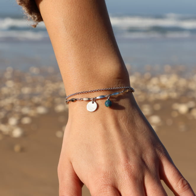 Bracelet en métal argenté, perles vertes et touches multicolores, porté sur fond naturel.