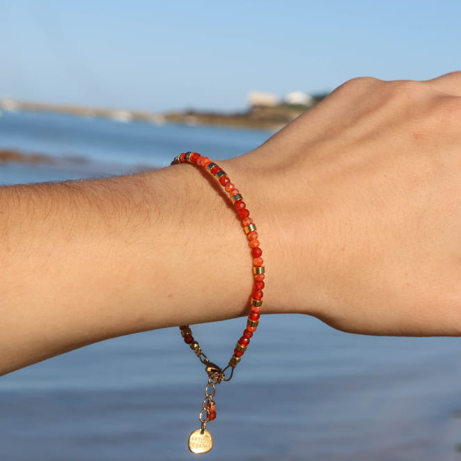 bracelet Clémentine doré avec perles orange porté au poignet sur fond marin