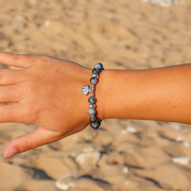 bracelet Konko argenté et noir porté au poignet sur fond sable