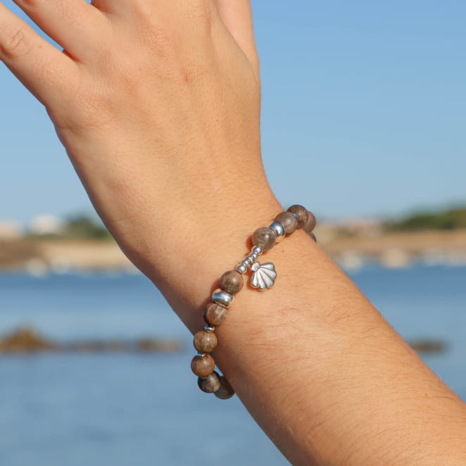 bracelet Konko argenté avec perles grises porté au poignet sur fond marin