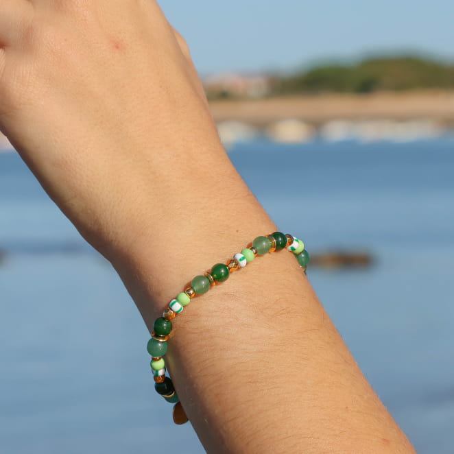 bracelet Martina doré avec perles vertes porté au poignet en bord de mer