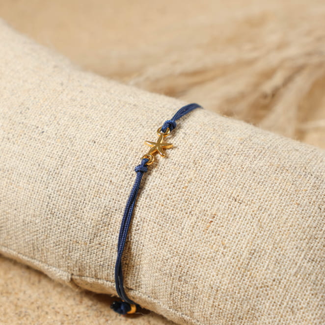 bracelet Transat doré avec cordon bleu marine posé sur tissu clair
