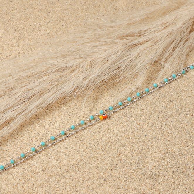 bracelet de cheville Bonita argenté avec perles bleues, posé sur sable doré