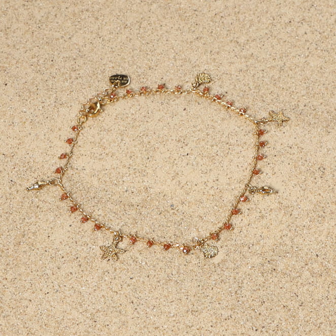 bracelet de cheville Ponta doré avec perles terracotta posé sur tissu clair