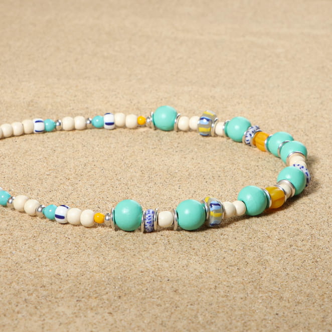 collier Bariolé argenté avec perles émeraude et multicolores sur sable clair