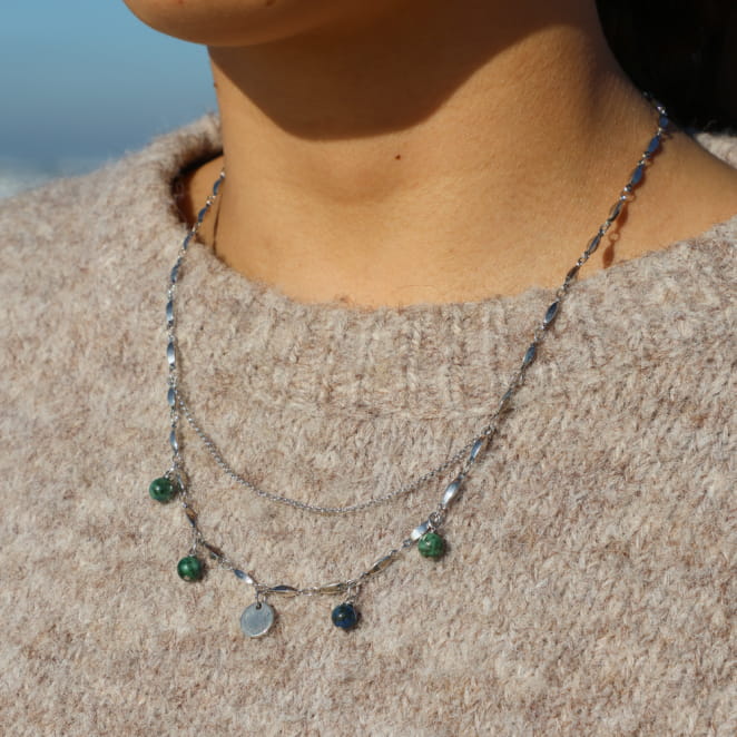 Collier argenté à perles vertes et accents multicolores, porté sur un pull côtelé beige.