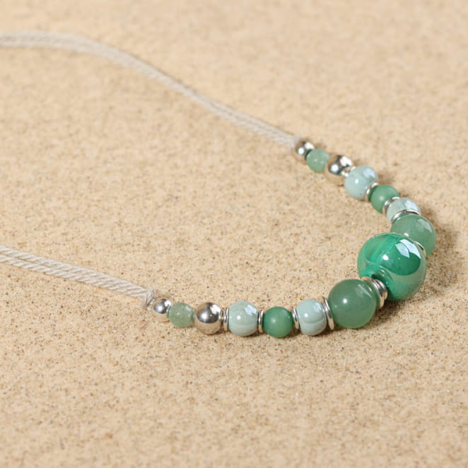 Collier Pascala argenté, perles vert d’eau et touches multicolores, posé sur le sable – bijou fait main en France