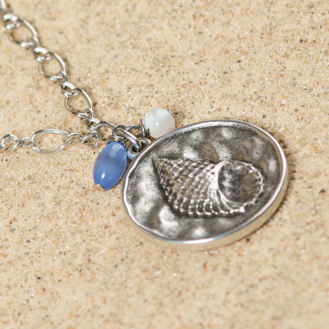 Gros plan sur le collier Pêche argenté et ses perles bleues, posé sur une coupelle – bijou délicat français