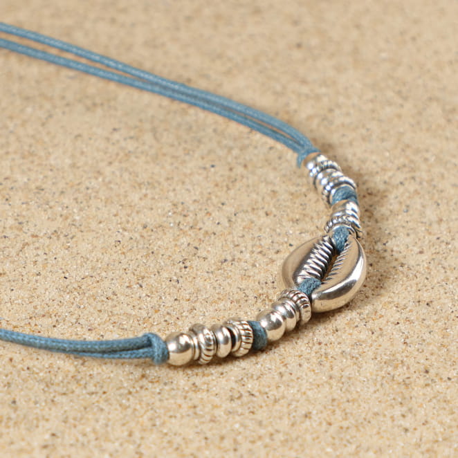 Détail du collier Seignosse avec pendentif cauri en métal argenté, perles argentées et cordon bleu montana, fermoir mousqueton et médaille Retour de Plage – création artisanale française élégante