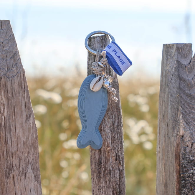 porte-clés Pilou argenté et bleu accroché sur bois
