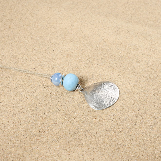 sautoir Douhet argenté orné de perles bleu Montana posé sur tissu clair