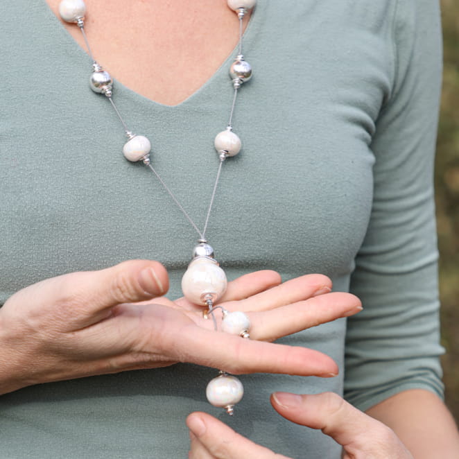 Sautoir Patèl blanc et argenté porté sur un pull gris – bijou long élégant