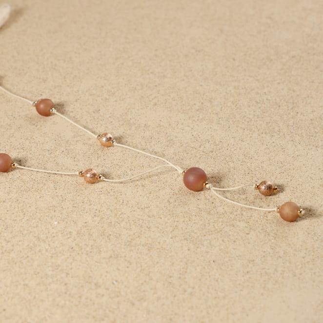 Sautoir Rosée doré rose saumon posé à plat, montrant son design élégant avec perles d'agate druzy et médaille Retour de Plage doré rose.