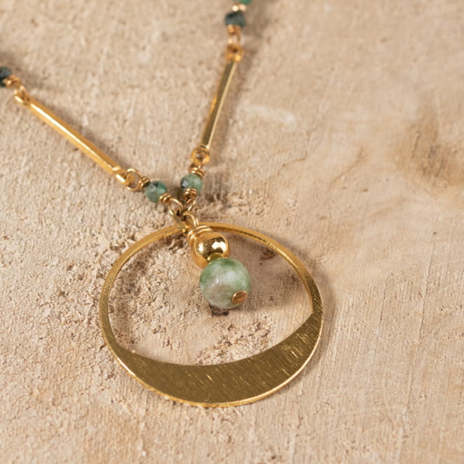 Zoom sur pendentif du sautoir Molly vert et doré, posé sur le sable – fabrication française